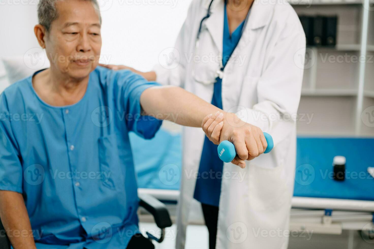 Asian physiotherapist helping elderly man patient stretching arm during exercise correct with dumbbell in hand during training hand in bed in clinic photo