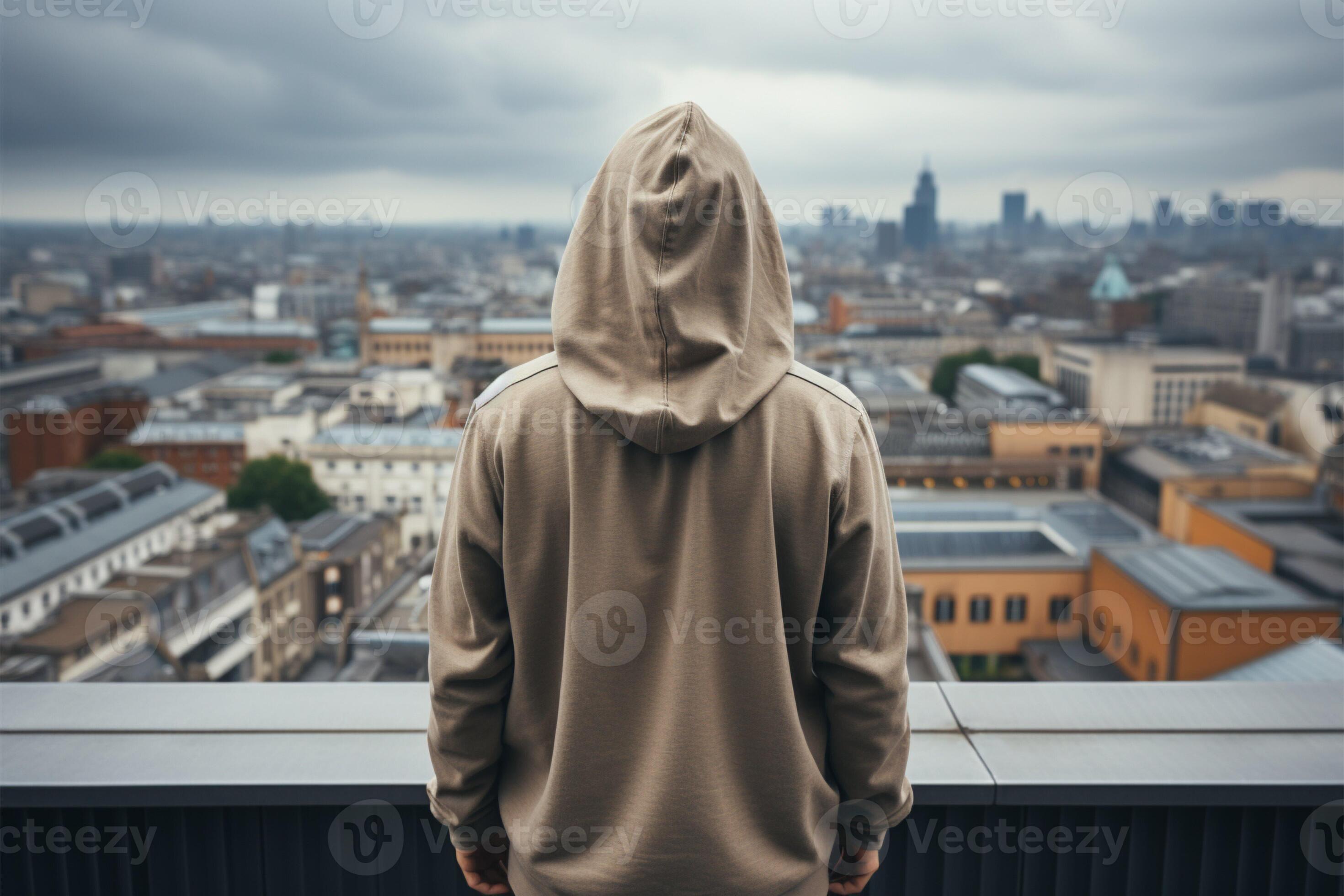 Man in hood stands aloof on rooftop, face concealed, blank space