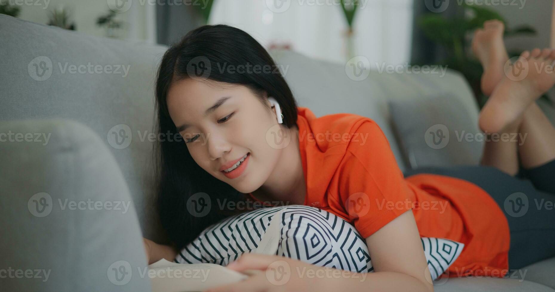 asiático mujer leyendo un libro mientras acostado en el sofá foto