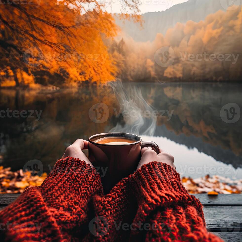 a person holding cup of coffee in the hands in front of lake photo