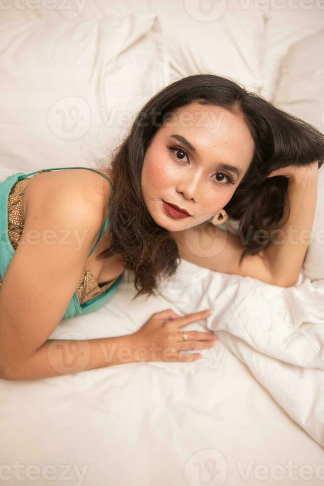 un asiático mujer en un verde vestir es dormido en un blanco cama en un lujo hotel foto