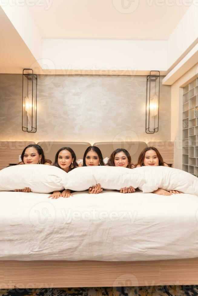 a group of Asian women are sleeping and leaning on white pillows with their friends in a luxury hotel photo