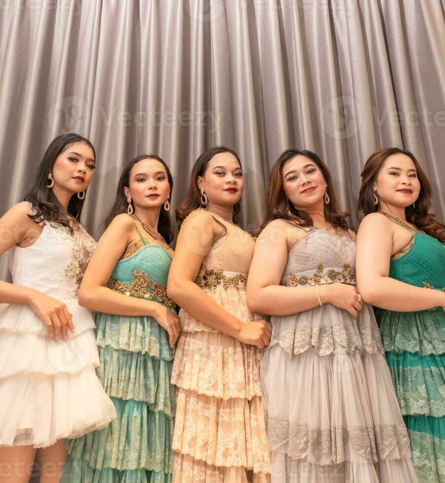 a group of Asian women are standing in front of the curtains of a luxury hotel while wearing dresses at a party photo