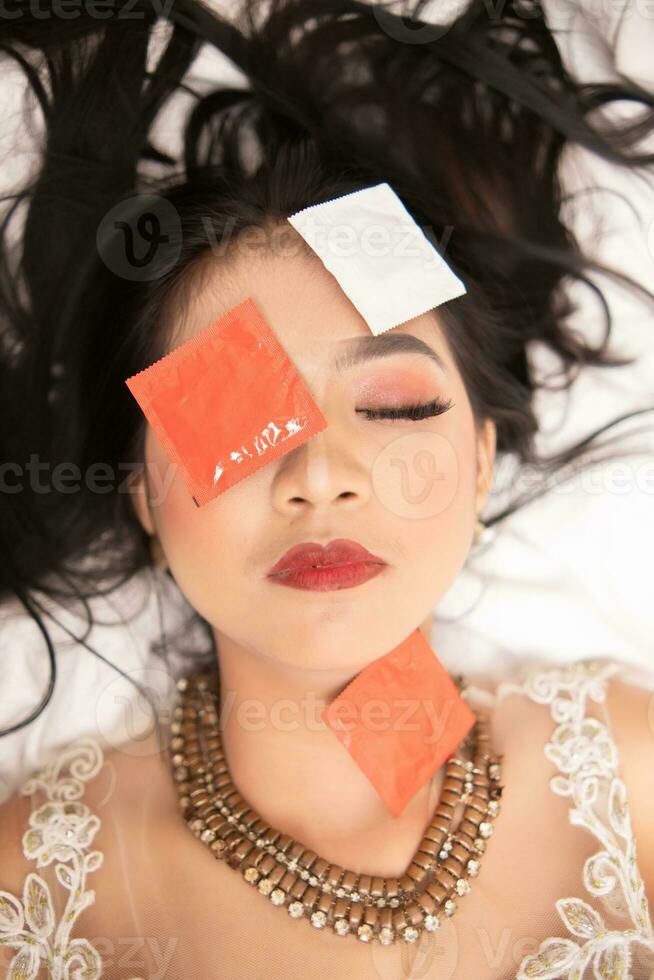 an Asian woman with a gold necklace falls asleep with a condom wrapper on her face in a hotel photo