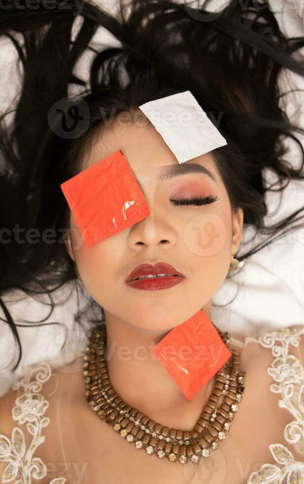 an Asian woman with a gold necklace falls asleep with a condom wrapper on her face in a hotel photo