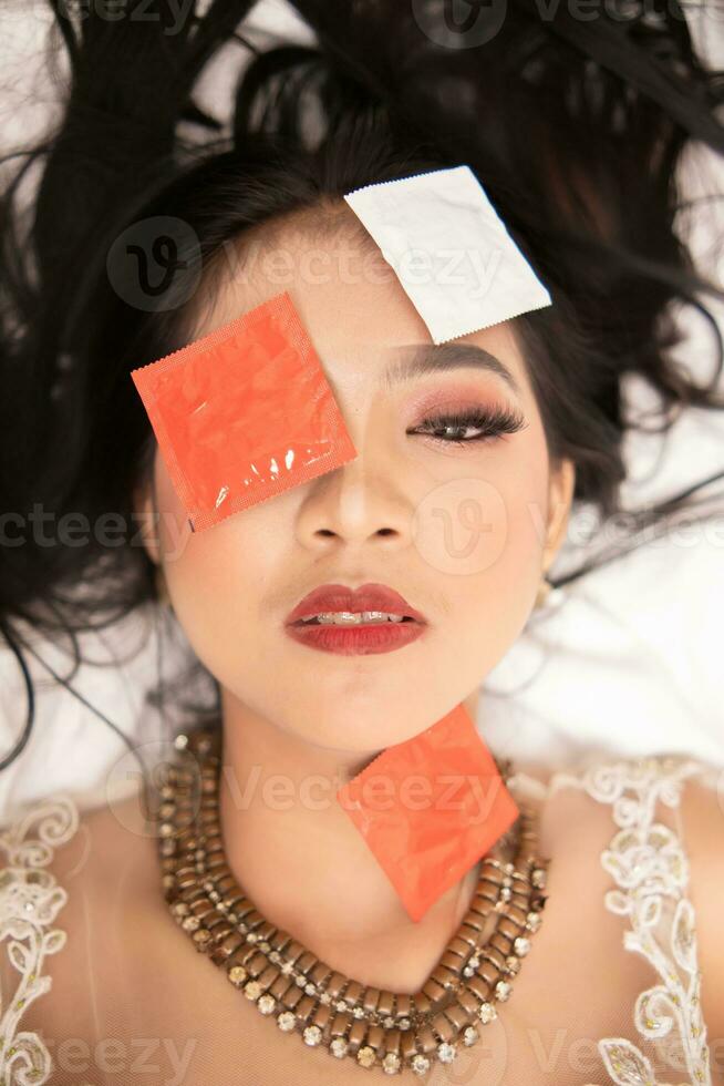 an Asian woman with a gold necklace falls asleep with a condom wrapper on her face in a hotel photo