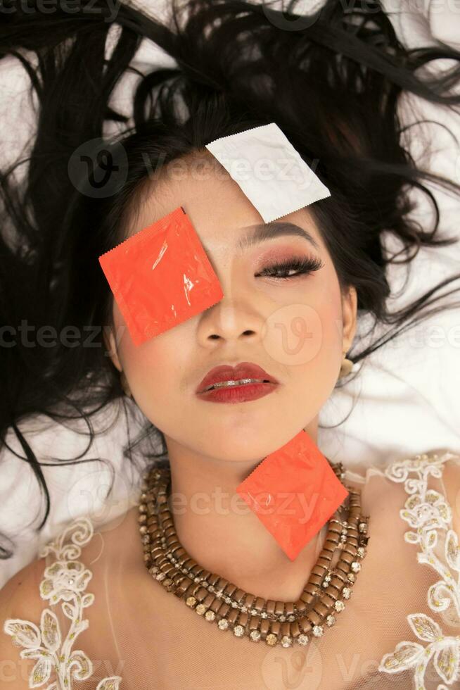 an Asian woman with a gold necklace falls asleep with a condom wrapper on her face in a hotel photo