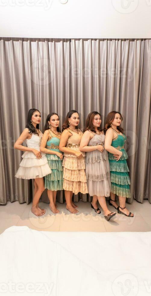 a group of Asian women are standing in front of the curtains of a luxury hotel while wearing dresses at a party photo