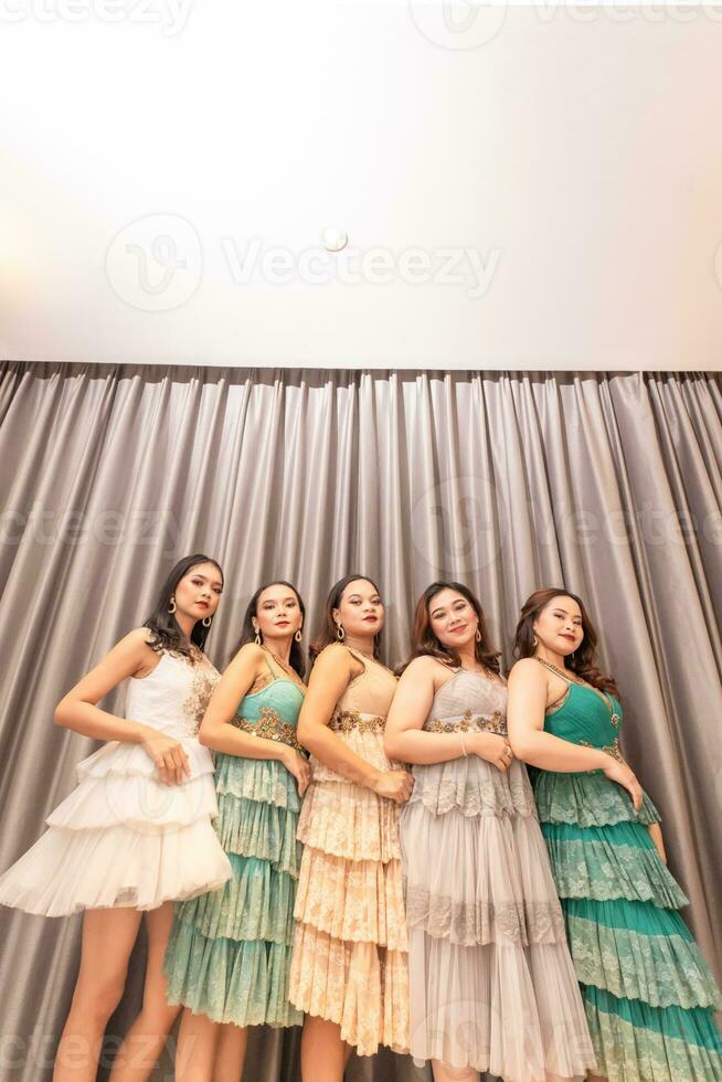 a group of Asian women are standing in front of the curtains of a luxury hotel while wearing dresses at a party photo