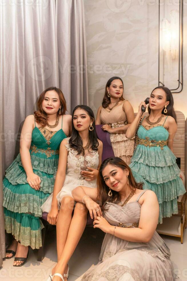 a group of Asian women in luxurious dresses are waiting for dinner in a hotel ballroom photo