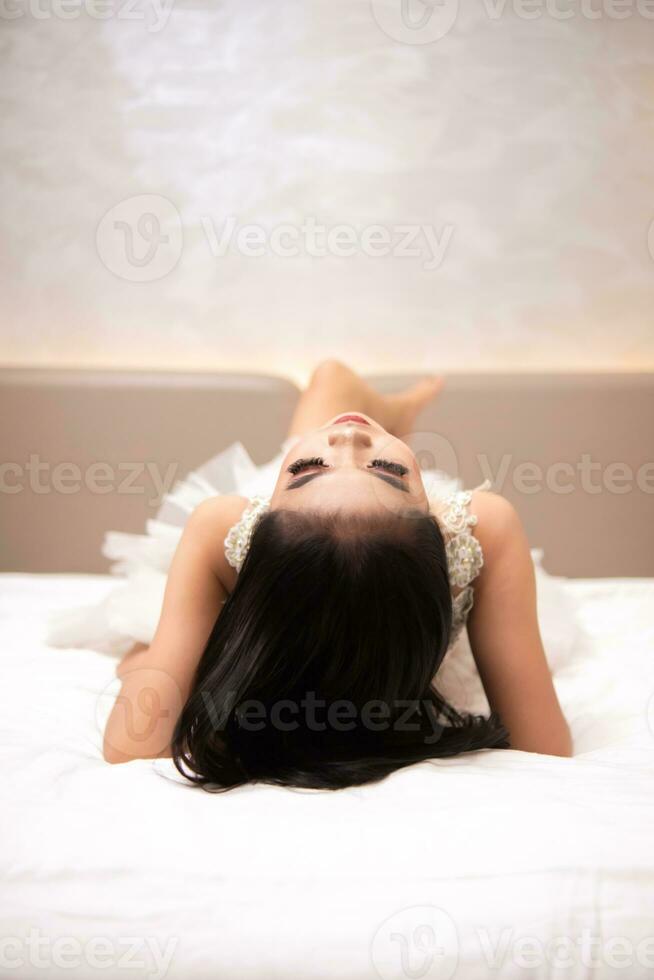 an Asian woman with black hair is sleeping on a white bed in an elegant hotel photo