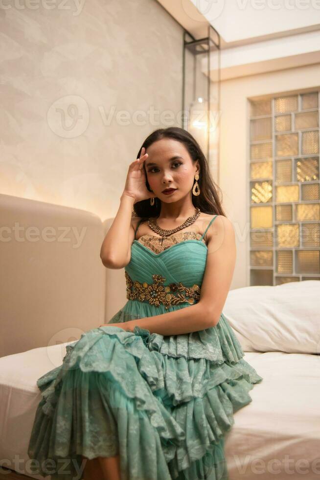 un asiático mujer con un oro collar y pendientes es posando hermosamente en un hotel habitación antes de cena foto