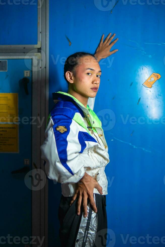 a gay Asian man posing in a tracksuit in front of a blue locker photo