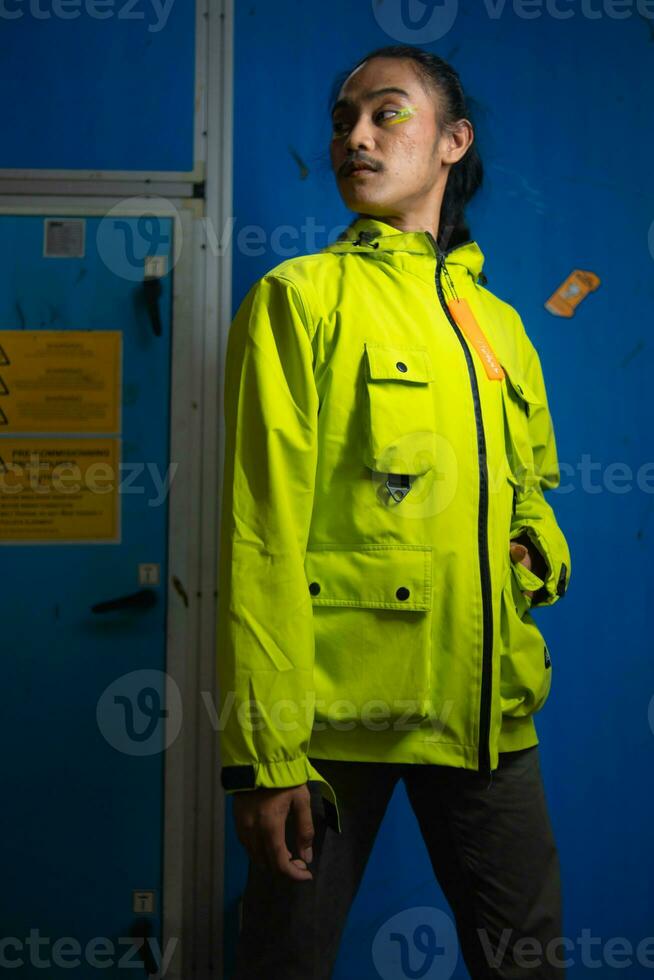 an Asian man in a green jacket is posing in front of a blue door photo