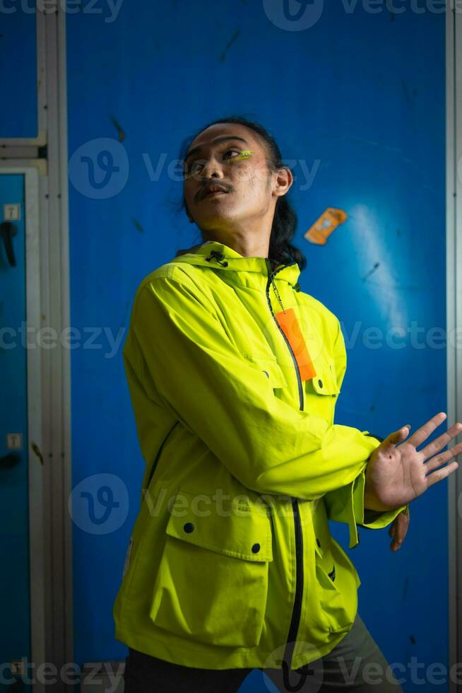 an Asian man in a green jacket is posing in front of a blue door photo