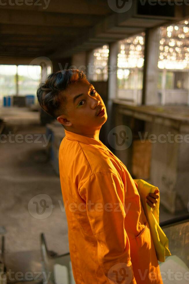 an Asian man standing in front of the window of an abandoned building while wearing a yellow blazer photo