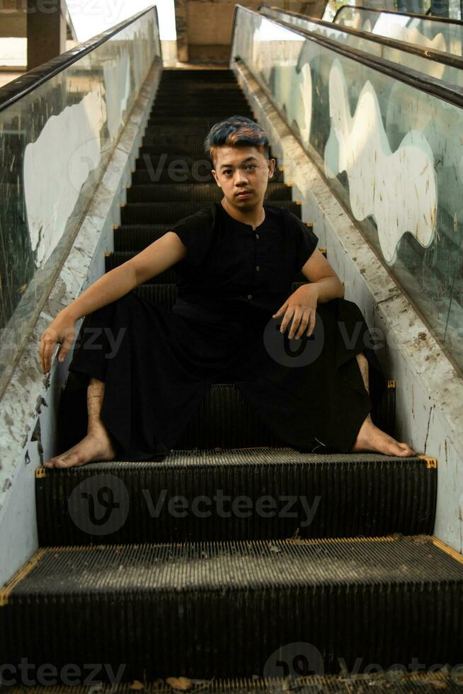 an Asian man in black clothes is sitting in a broken and abandoned elevator in an old building photo