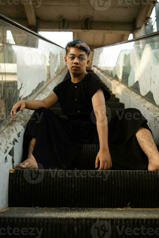 an Asian man in black clothes is sitting in a broken and abandoned elevator in an old building photo