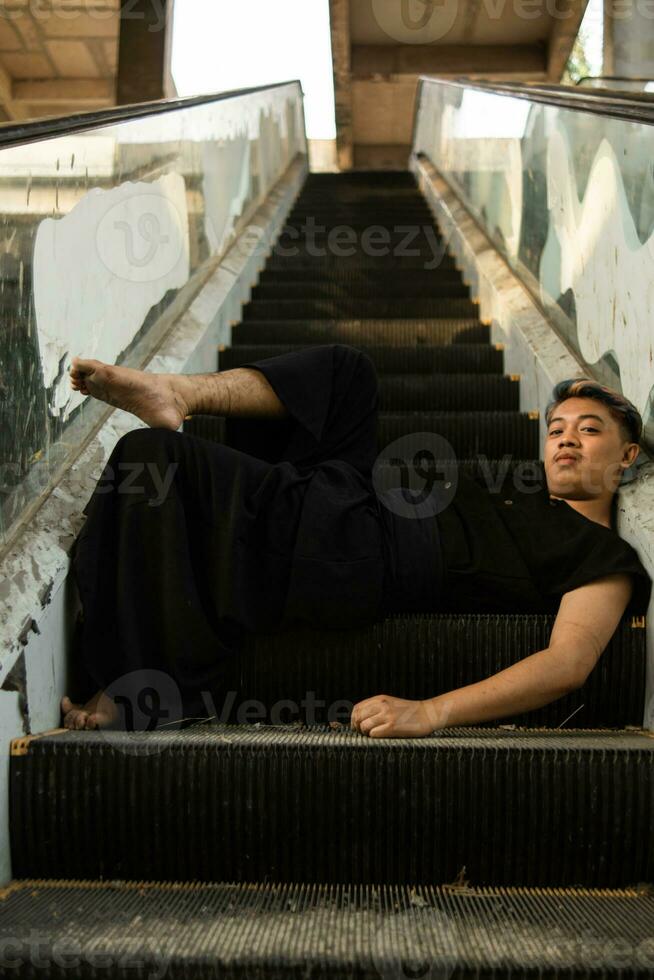 an Asian man in black clothes is sitting in a broken and abandoned elevator in an old building photo