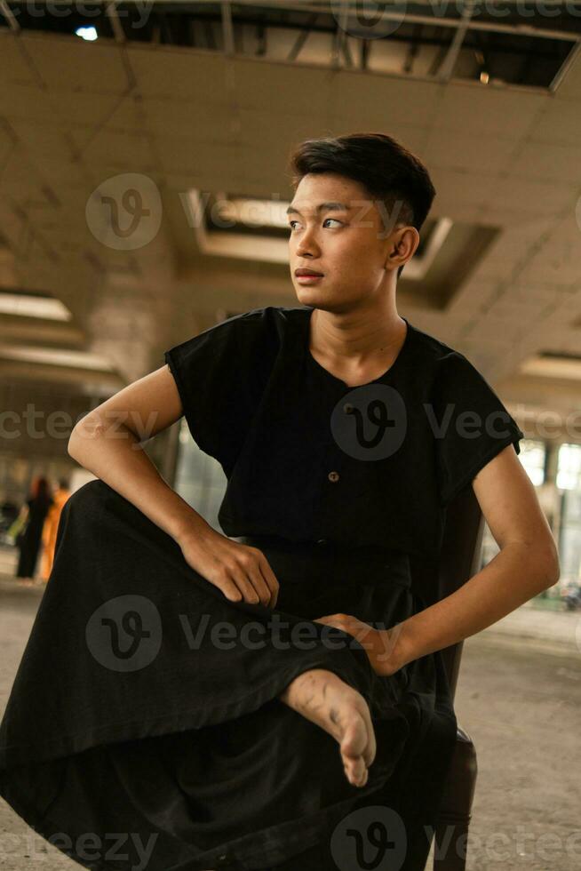 an Asian man in a black shirt is sitting on a brown wooden chair photo