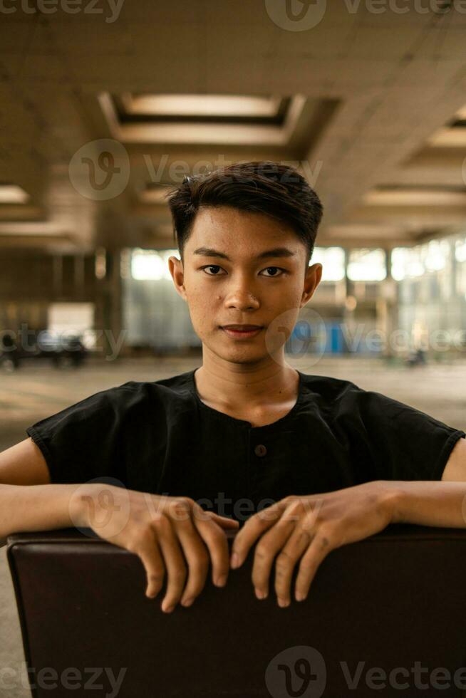 an Asian man posing on a brown leather chair while wearing black pants in an old building photo