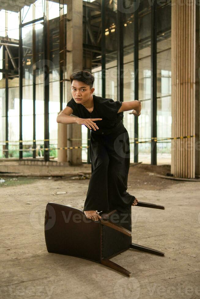 an Asian man is standing on a wooden chair while wearing a black dress in an old building photo