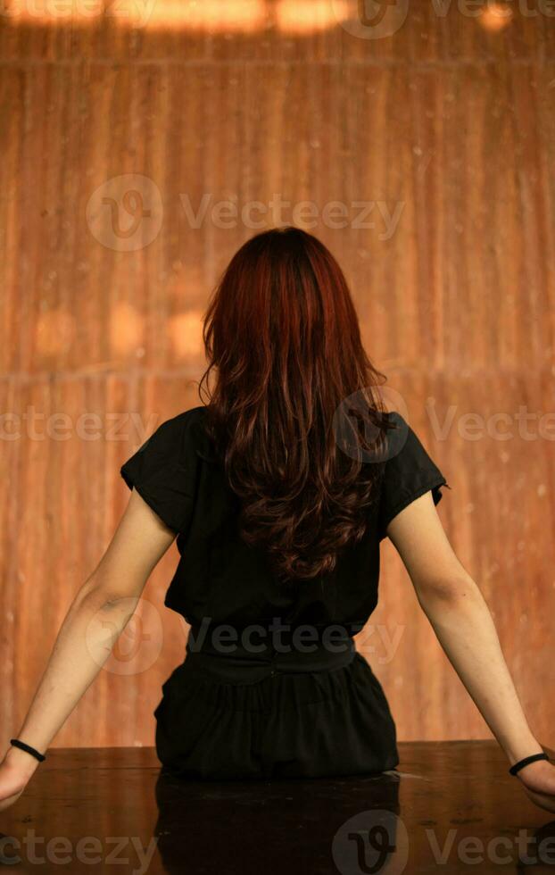 an Asian man with long hair is sitting in front of a brown wooden background photo