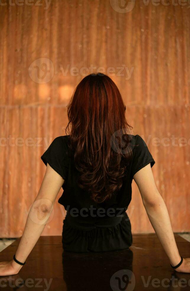 an Asian man with long hair is sitting in front of a brown wooden background photo