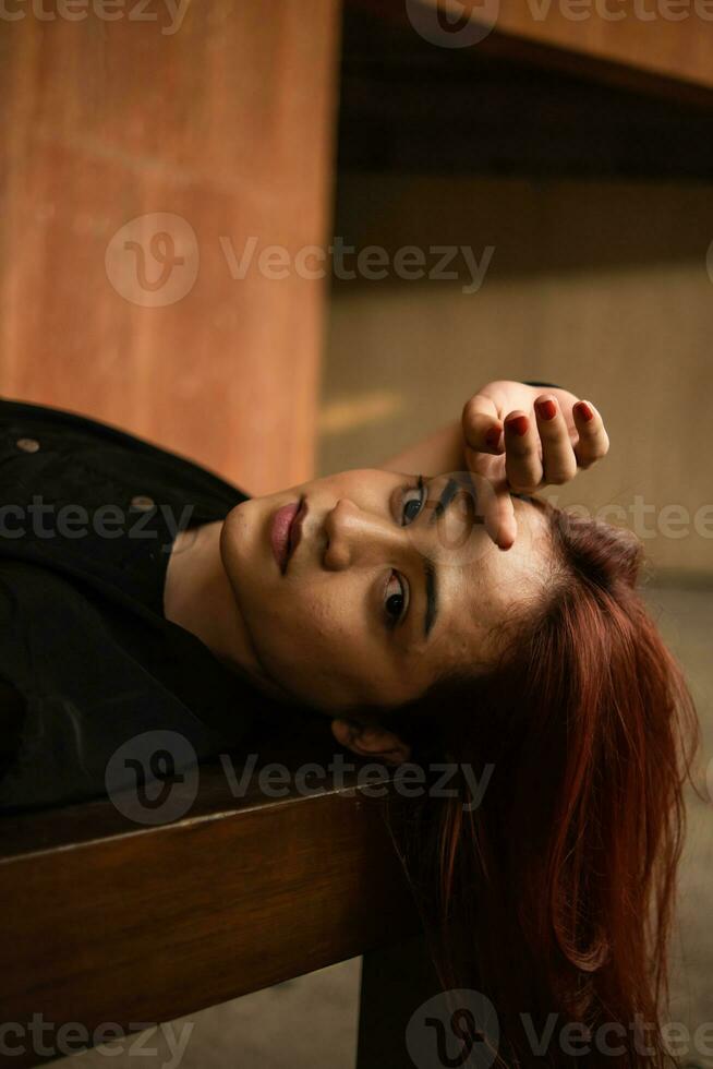 an Asian man sleeping on a brown table with long hair hanging down photo