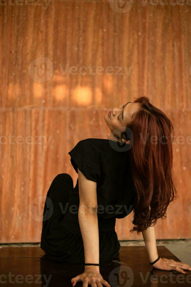 an Asian man is playing with his long hair with his hands while sitting in a wooden house photo