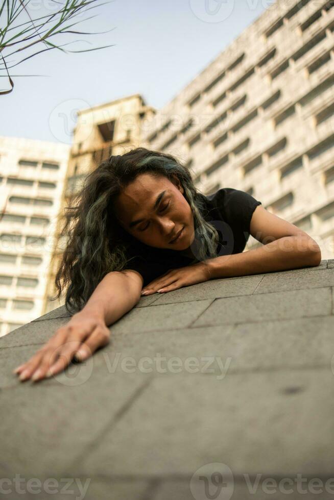 un asiático hombre duerme en un mármol rock mientras vistiendo negro ropa alrededor un antiguo edificio foto