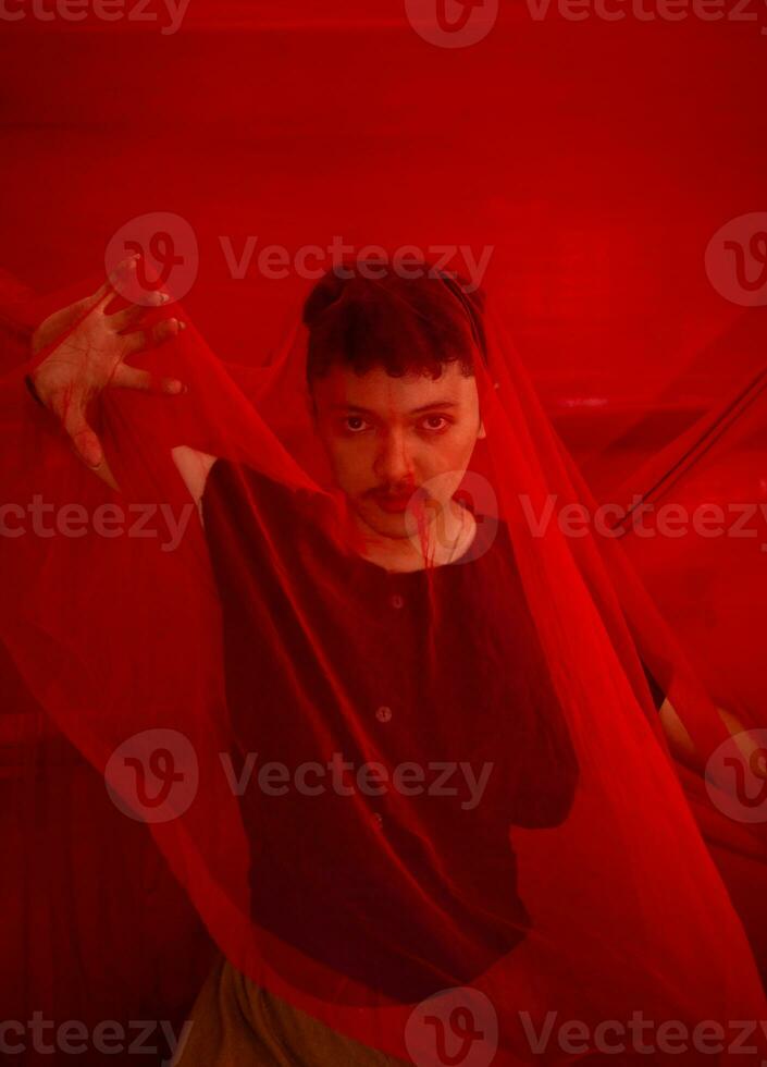 an Asian man in a black shirt covering his face with a red cloth with a frightening facial expression in front photo