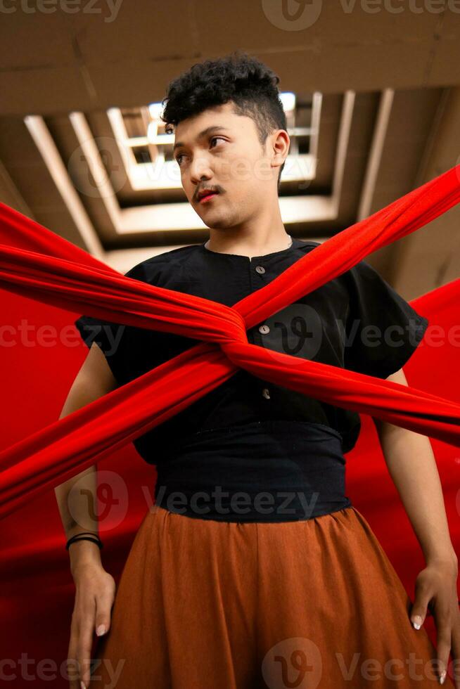 un asiático hombre soportes debajo el ligero como su cuerpo es ligado por un rojo paño foto