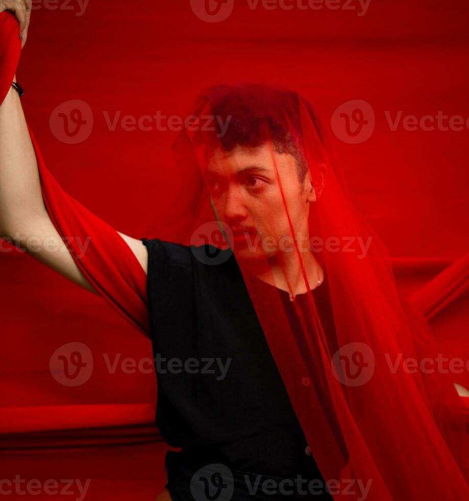 an Asian man in a black shirt covering his face with a red cloth with a frightening facial expression in front photo