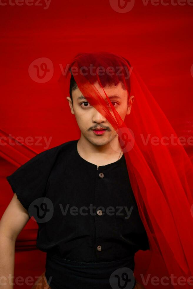 an Asian man standing in front of a red cloth with a red cloth hanging over his head photo