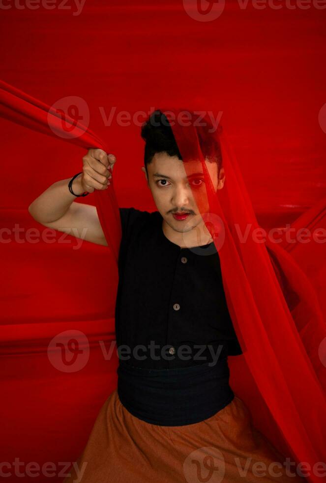 an Asian man in a black shirt covering his face with a red cloth with a frightening facial expression in front photo