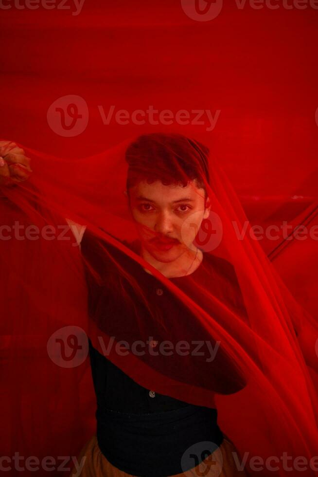 an Asian man in a black shirt covering his face with a red cloth with a frightening facial expression in front photo