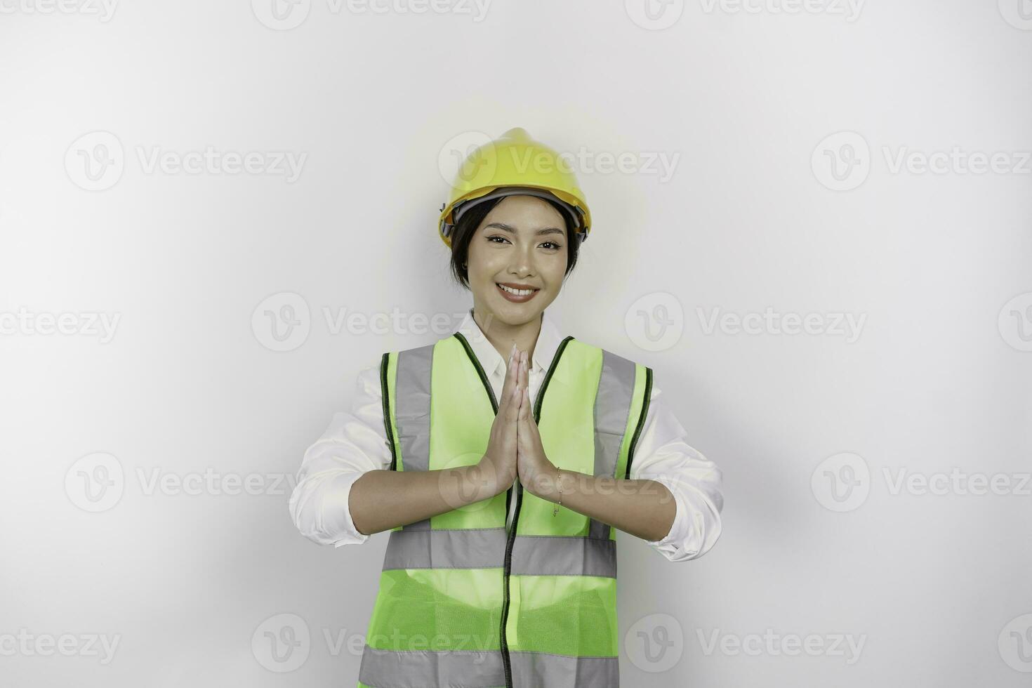 Friendly Asian woman labor worker in industry factory, gesturing traditional greeting, wearing yellow safety helmet, green vest and uniform, isolated white background. photo