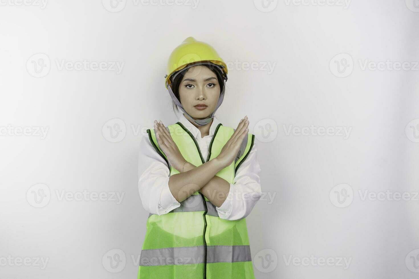 hermosa asiático mujer labor trabajador vistiendo un la seguridad casco y chaleco con mano gesticulando rechazo o prohibición aislado blanco antecedentes. mano de obra día concepto. foto