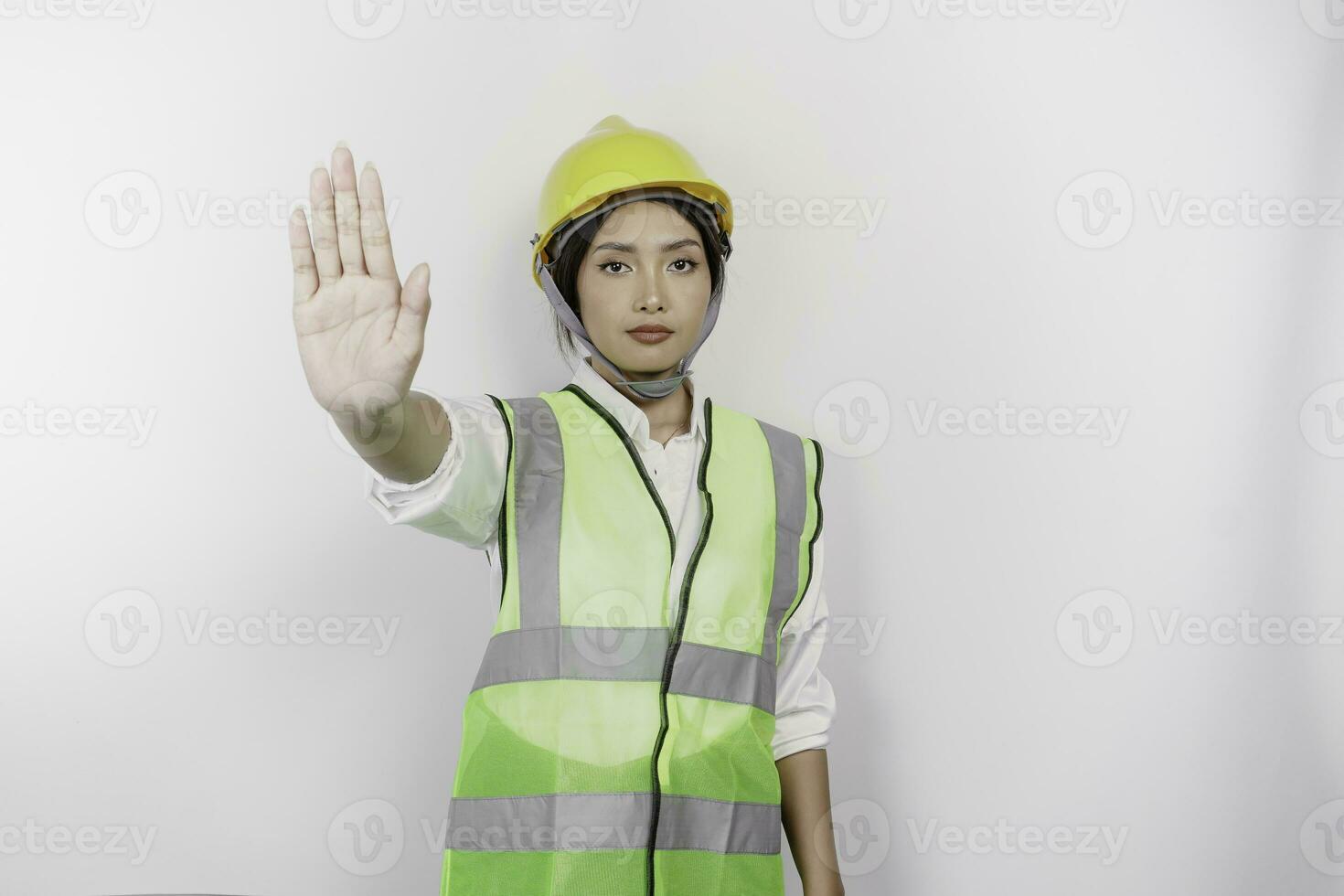 Serious Asian woman labor wearing safety helmet and vest with hand gesture pose rejection or prohibition, isolated by white background photo