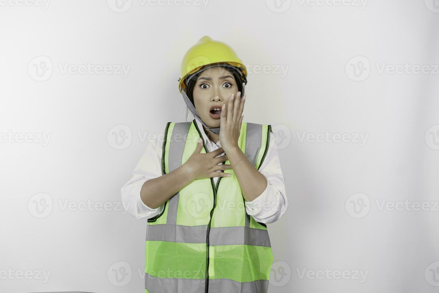 A portrait of a shocked Asian woman labor wearing safety helmet and vest while her mouth wide open, isolated by white background. Labor's day concept photo