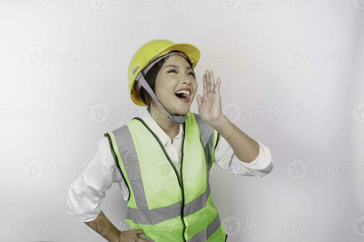 Young beautiful woman labor wearing safety helmet and vest is shouting and screaming loud with a hand on her mouth. Labor's day concept. photo