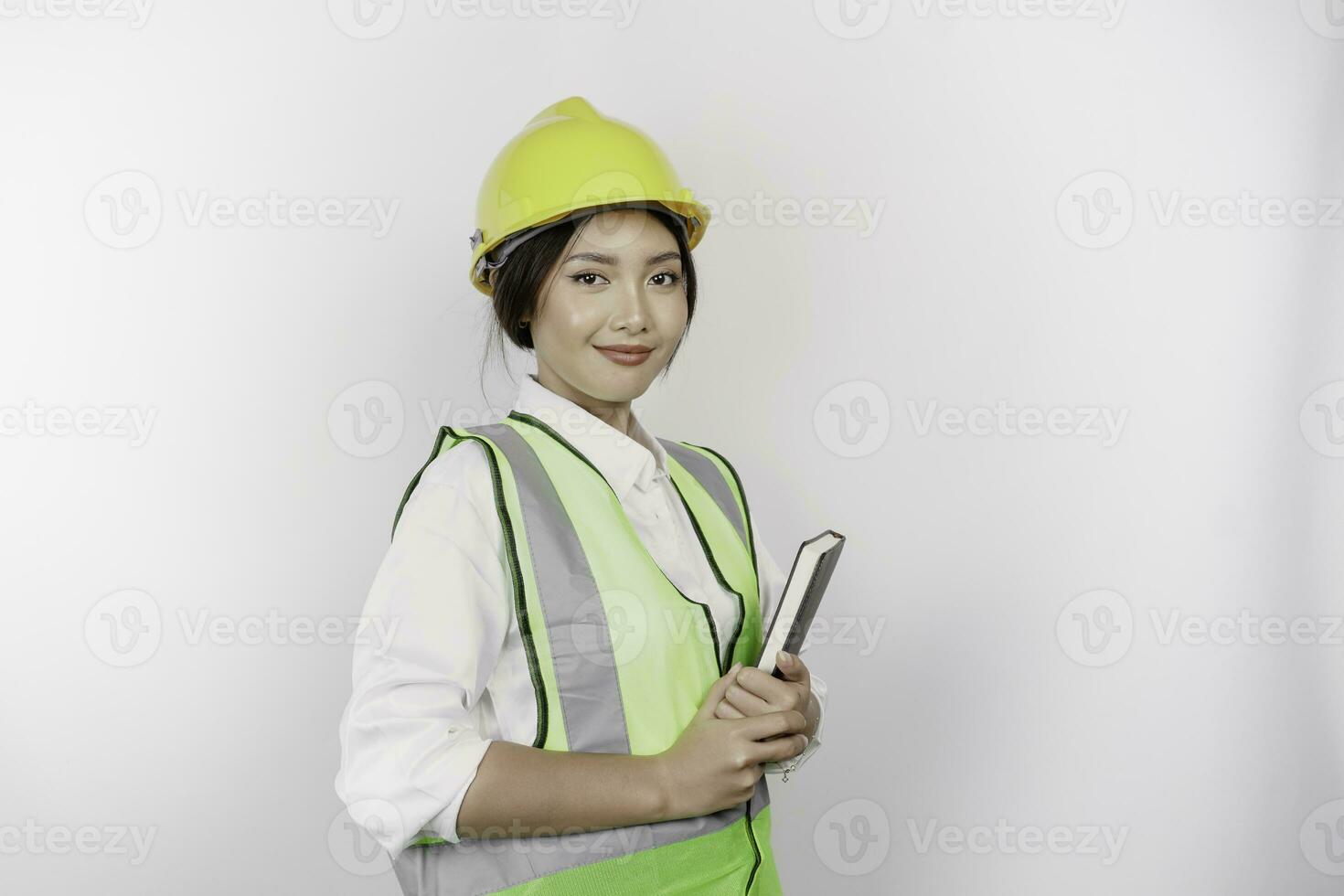 un sonriente asiático mujer labor vistiendo la seguridad casco y chaleco, participación su libro, aislado por blanco antecedentes. mano de obra día concepto. foto