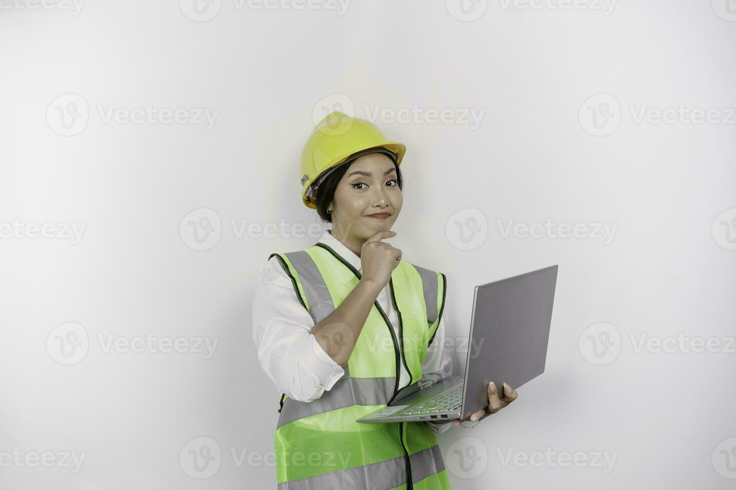 A thoughtful young woman labor worker wearing safety helmet and vest while holding her laptop and hand on her chin, isolated by white background. Labor's day concept. photo