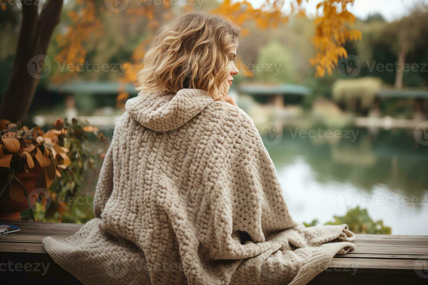 A beautiful girl sitting on a bench in the park, wearing a chunky crocheted poncho, cream colored yarn. Warmth and coziness concept. AI Generated. photo