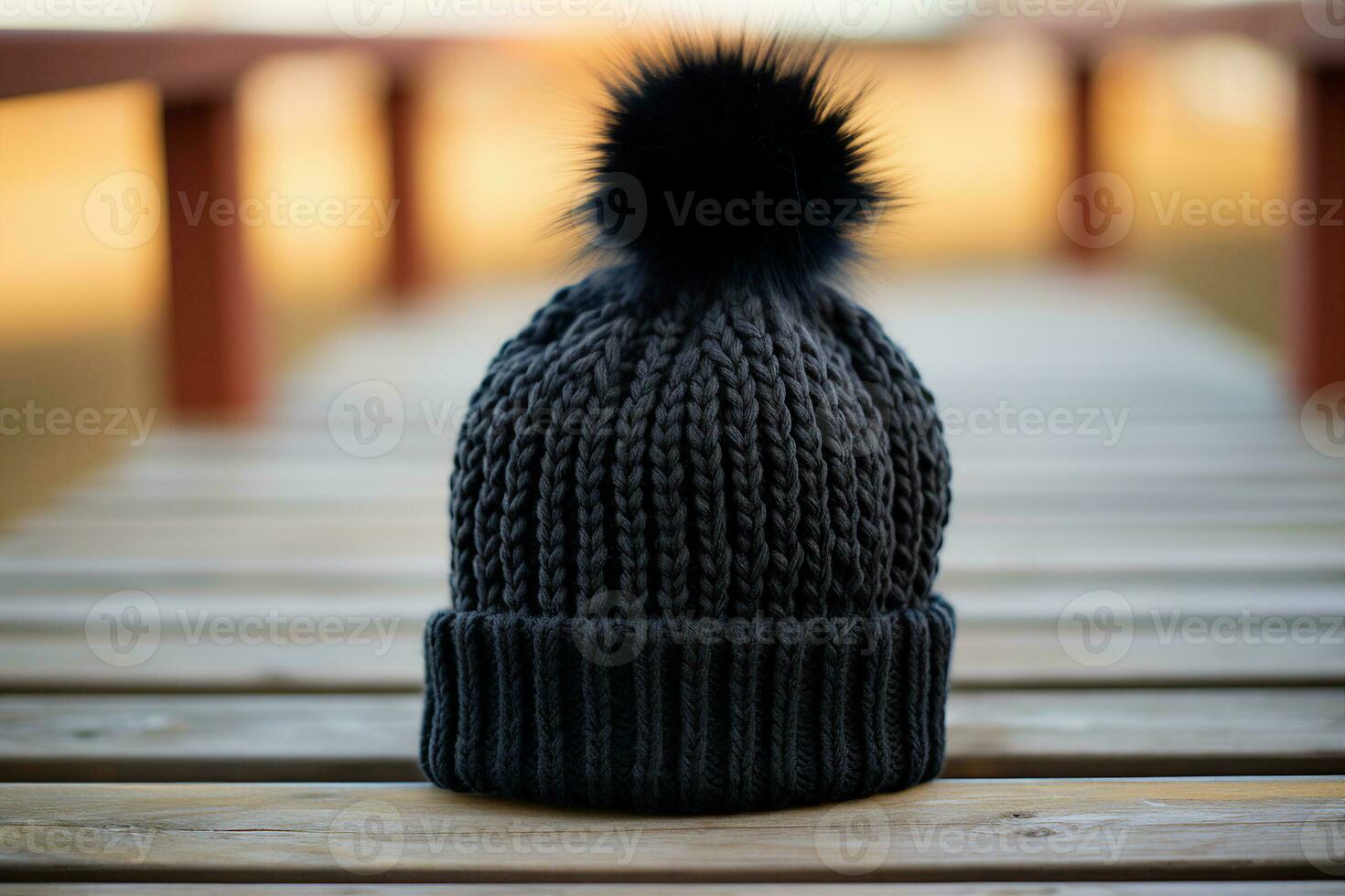 A close up view of a black crocheted beanie with a faux fur pompom, resting on a wooden surface, shallow depth of field. AI Generated. photo