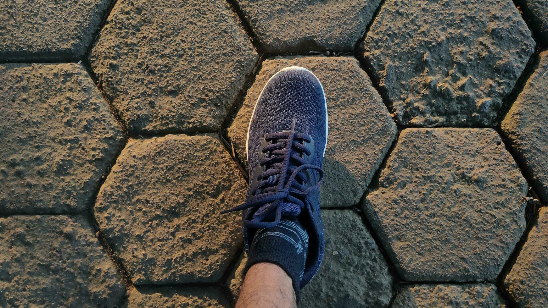 Close-up shot of feet wearing sneakers on a brick road lit by the rising sun. photo