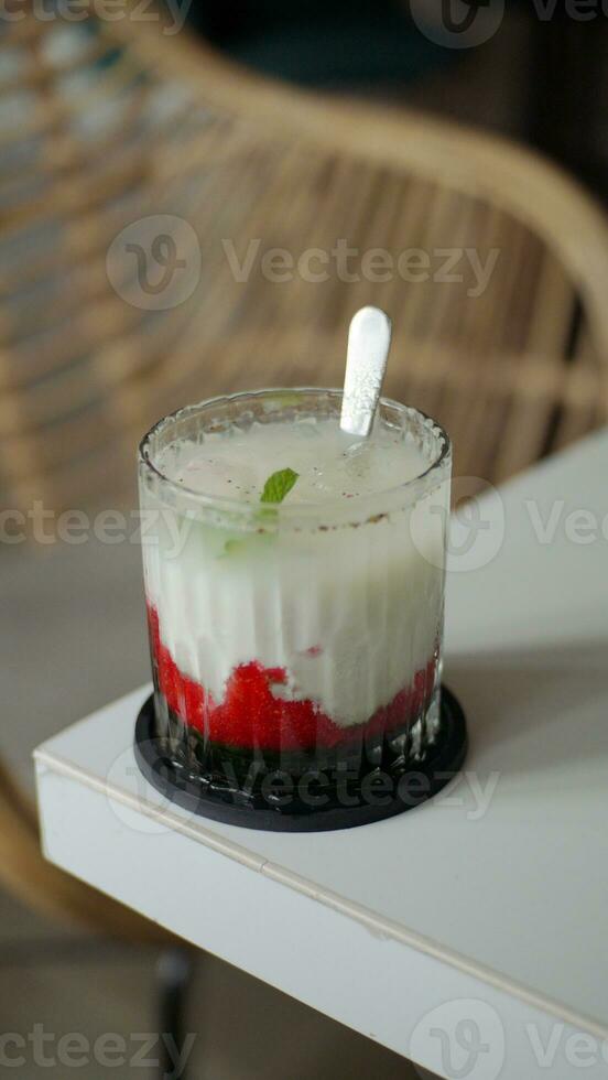 A glass of strawberry drink with milk and mint leaf topping on a white table in a cafe. photo