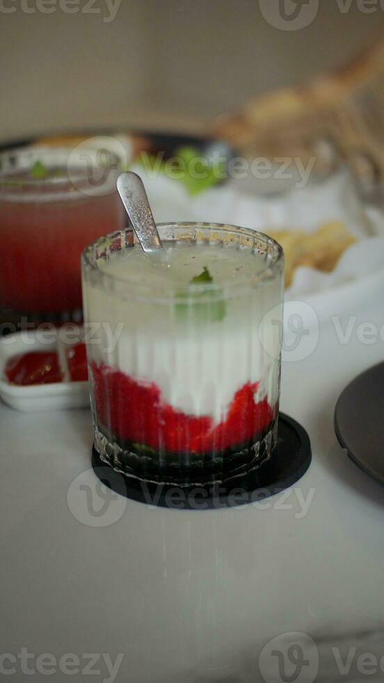 A glass of strawberry drink with milk and mint leaf topping on a white table in a cafe. photo