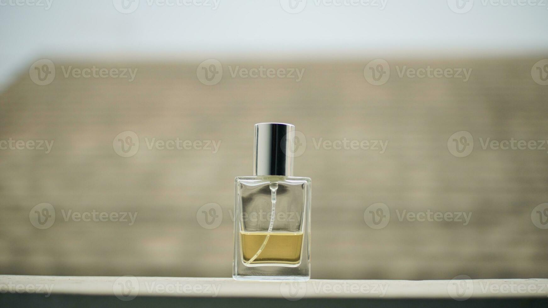 Small transparent perfume bottle filled with yellow liquid on table with minimalist blurry background. photo